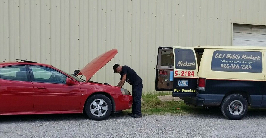 A mechanic working on a red car beside a van marked C&J Mobile Mechanic